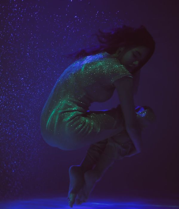 Woman in a calm yoga pose in a dark room with blue light.